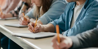 一排多民族学生在教室里考试的移动镜头。专注于拿笔和在笔记本上写作。聪明的年轻人在大学学习。