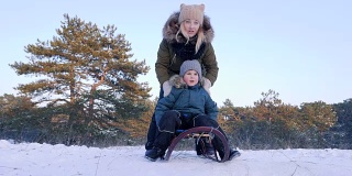 一家人在冬天的森林里休息，妈妈在新鲜的空气中推着快乐的儿子在雪橇上