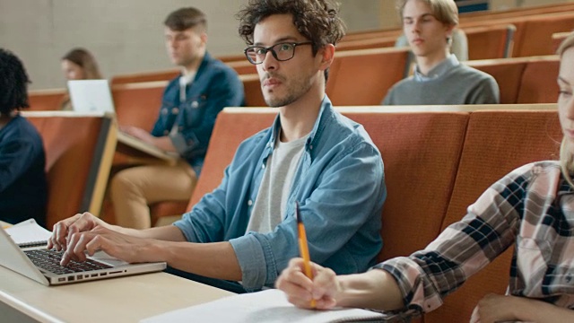 在多民族学生的课堂上，在听讲师讲课时使用笔记本电脑。有些人在笔记本上写字。聪明的年轻人在大学学习。