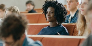 聪明美丽的年轻黑人女孩在一间满是多民族学生的教室里听讲座。浅景深。