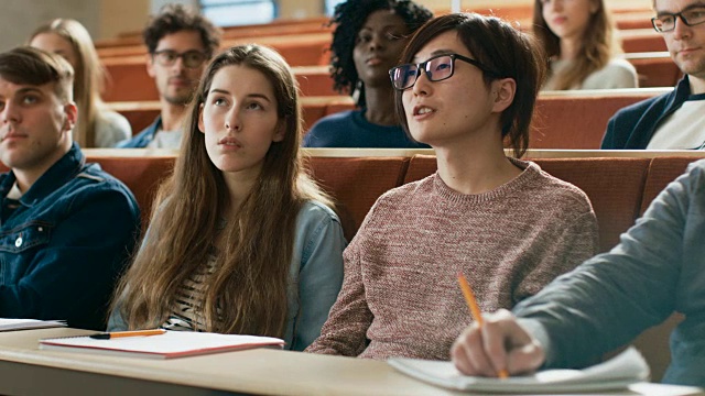 在教室里聪明的亚洲学生问教授一个问题。多元种族的现代聪明学生在学院。