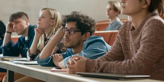 无聊男学生在大学听讲座。疲惫，疲惫和过度工作的年轻男性。