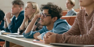 一群无聊的学生在大学听讲座。疲惫，疲惫和过度工作的年轻男性。