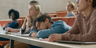 疲惫的男学生在大学演讲时睡觉。劳累过度的年轻男性。