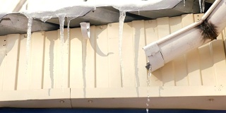 屋顶上有冰柱，水从排水管中流出。春天解冻。