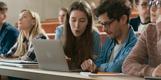 在教室里男女同学分享和使用笔记本电脑，在课堂上聊天。正在学习的年轻人。大学的生活。