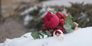 婚礼花束和结婚戒指，红色的花在雪的背景