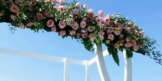 婚礼装饰，白色的婚礼拱门装饰着玫瑰，在海滩上举行婚礼仪式，在海滩上准备婚礼仪式