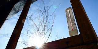 在太阳的背景下，放在窗户上的温度计。美丽的太阳眩光。温度高于零