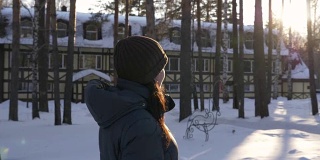 一个年轻女子走在冬天的村舍里，周围是桦树和松树。太阳闪耀光芒。