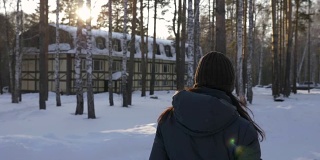 女人走在冬天的村舍，而阳光明媚的天气后视图