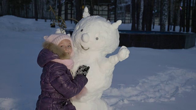 快乐的小女孩拥抱雪人在晚上冬天在乡村散步