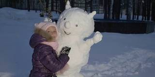 快乐的小女孩拥抱雪人在晚上冬天在乡村散步