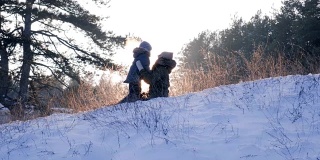 快乐的冬天休息，妈妈和儿子在雪地上背光玩在森林背景美丽的自然