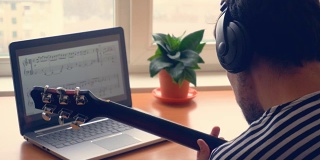 戴着耳机的男人在窗前用笔记本电脑弹着电吉他