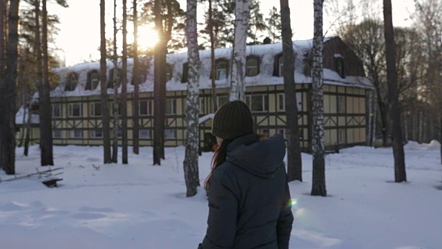 在冬日的阳光下漫步在白雪覆盖的公园里的女人