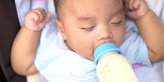 婴儿在婴儿车里吃奶瓶里的牛奶