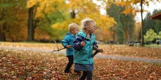 孩子们在秋叶上走，拿着树枝