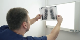 成年医生手里拿着一张x光照片，讨论着。一个穿着医生衣服的男人正在检查医院医疗设备上的一张照片