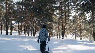 在阳光明媚的冬日里，小男孩拉着雪橇上山。视频素材模板下载
