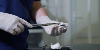 戴无菌手套的男医生在手术前从包装袋中取出医用纸巾并插入钳夹。在没有病人的诊所和医院里，用医疗器械和设备拉近外科医生的手