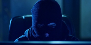 用面具破解密码的黑客…黑客带着面具用电脑从黑客暗室破解互联网。从屏幕上可以看到黑客的脸。红色电影摄像机拍摄。