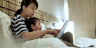 亚洲母亲和儿子在床上看书