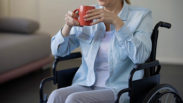老年妇女坐在轮椅上喝茶，退休老人在家里放松，休闲