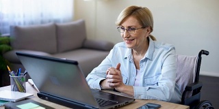 轮椅上的成功资深女性用笔记本电脑工作，和客户聊天