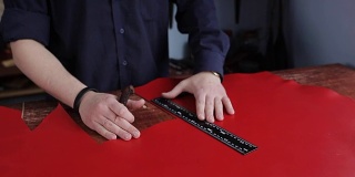 制革厂的制革工正在测量和切割红色的皮革
