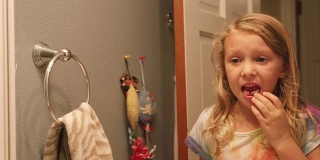 一个小女孩掉了一颗牙后，在浴室的镜子里晃动着一颗松动的牙齿