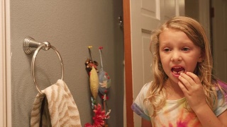 一个小女孩掉了一颗牙后，在浴室的镜子里晃动着一颗松动的牙齿视频素材模板下载