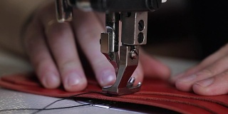 近距离拍摄的主人的手，谁使用缝纫机创造针在一个皮革钱包，针慢慢穿透材料
