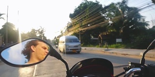 男子驾驶摩托车在热带岛屿在美丽的日落在缓慢的动作，而旅行。泰国。方向盘的视图。1920 x1080