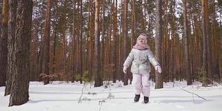 可爱的小女孩在冬天的森林里的雪地上跳跃，慢镜头