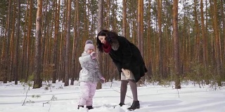 一名年轻女子和她的女儿站在冬天的森林里，向镜头挥手
