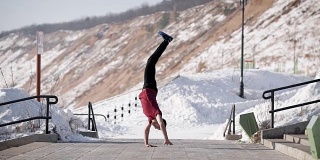 年轻肌肉发达的杂技演员在冬季的道路上双手站立和保持平衡的侧面图