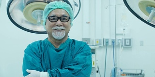 资深男医生看着镜头与迷人的微笑在手术室的背景。医学的概念