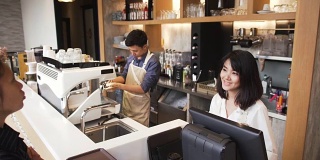 高角度视角:年轻的亚洲咖啡师在咖啡厅从女顾客那里获得咖啡订单