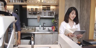 后视图:年轻的亚洲咖啡师在咖啡厅从女性顾客那里获得咖啡订单