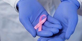 双手戴着手套小心翼翼地握着粉红丝带，象征对乳腺癌的关注