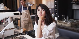 正面:年轻的亚洲咖啡师看着镜头，就好像她在看你
