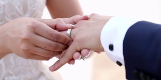 在海滩婚礼上，新娘把结婚戒指戴在新郎的手指上。