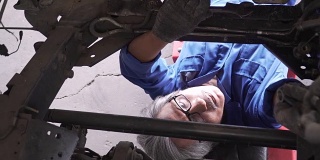 俯视图由小车拍摄:亚洲高级汽车技师在车辆下工作