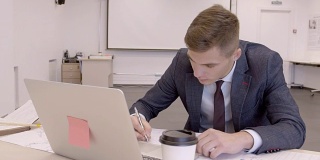 这是一幅年轻商人在办公室里用纸张和电脑绘制图表的慢镜头
