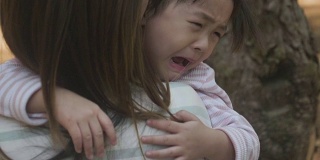 消极情绪亚洲母亲抱着哭泣的女婴在花园
