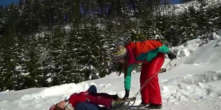 快乐的家庭在冬天的雪山森林里玩耍。妈妈和她的两个孩子在玩雪橇。他们笑了。