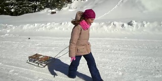 一个快乐的女孩在冬天的山上跑过一片雪林。她是笑。她身后拖着雪橇。