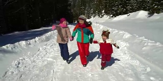 快乐的家庭在冬天的雪山森林里玩耍。妈妈和她的两个孩子在玩雪橇。他们笑了。