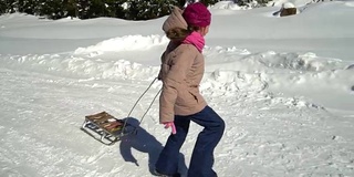 一个快乐的女孩在冬天的山上跑过一片雪林。她是笑。她身后拖着雪橇。缓慢的运动。